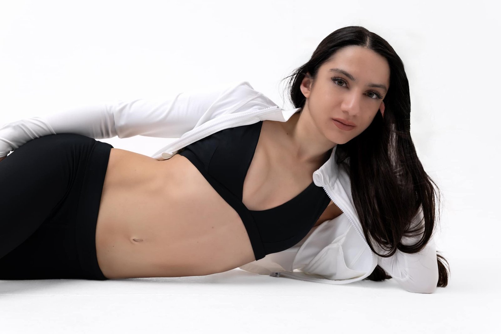 Side view of Petite Aesthetics black sports bra with white jacket on floor showing dynamic comfort and secure fit for petite women